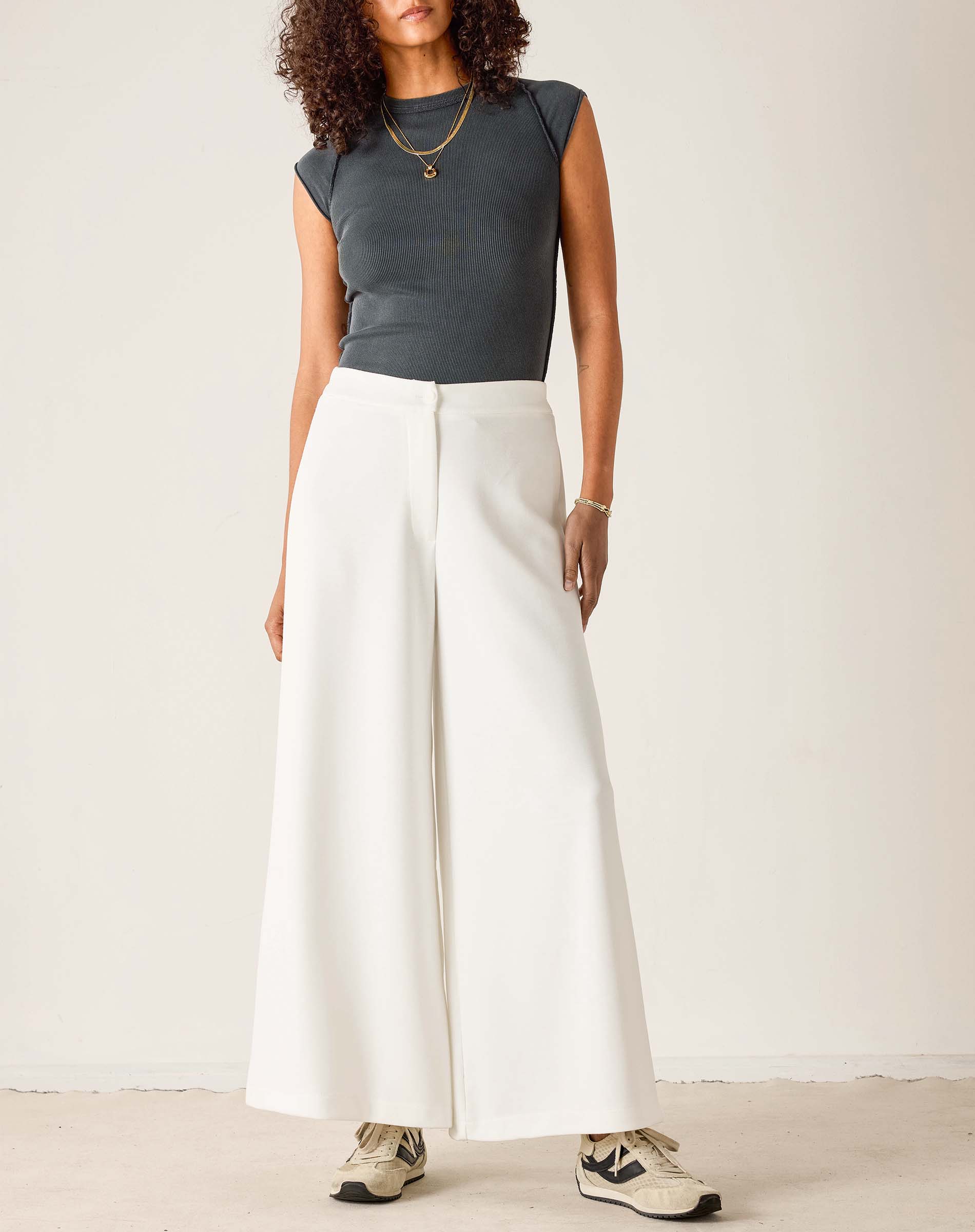 Person wearing a dark gray sleeveless top and white wide-leg pants on a plain background
