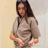 Woman wearing a beige outfit against a textured wall.