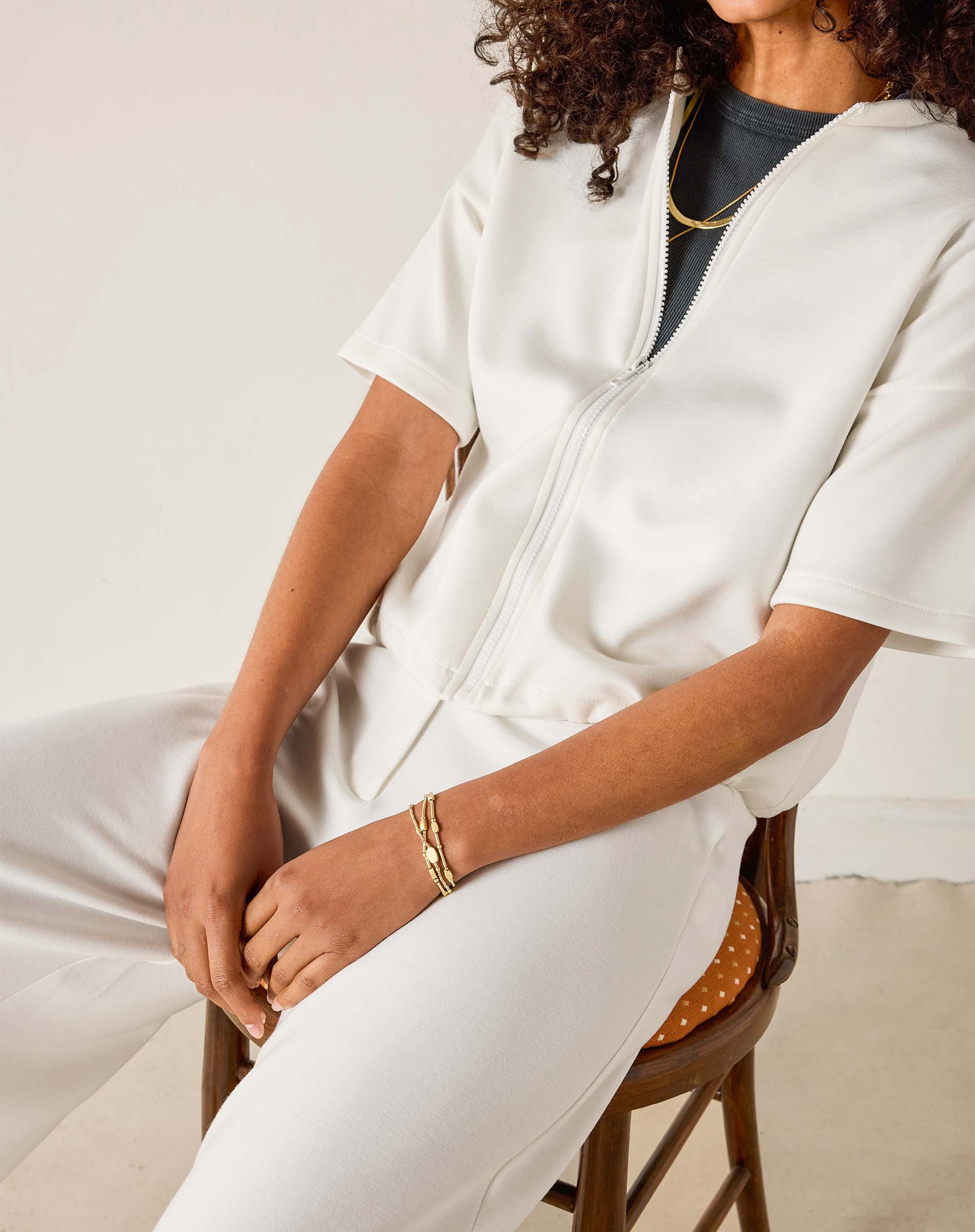 Person wearing a white outfit sitting on a chair with a neutral background