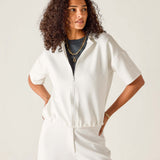 Woman wearing a white zip-up top and pants against a plain background