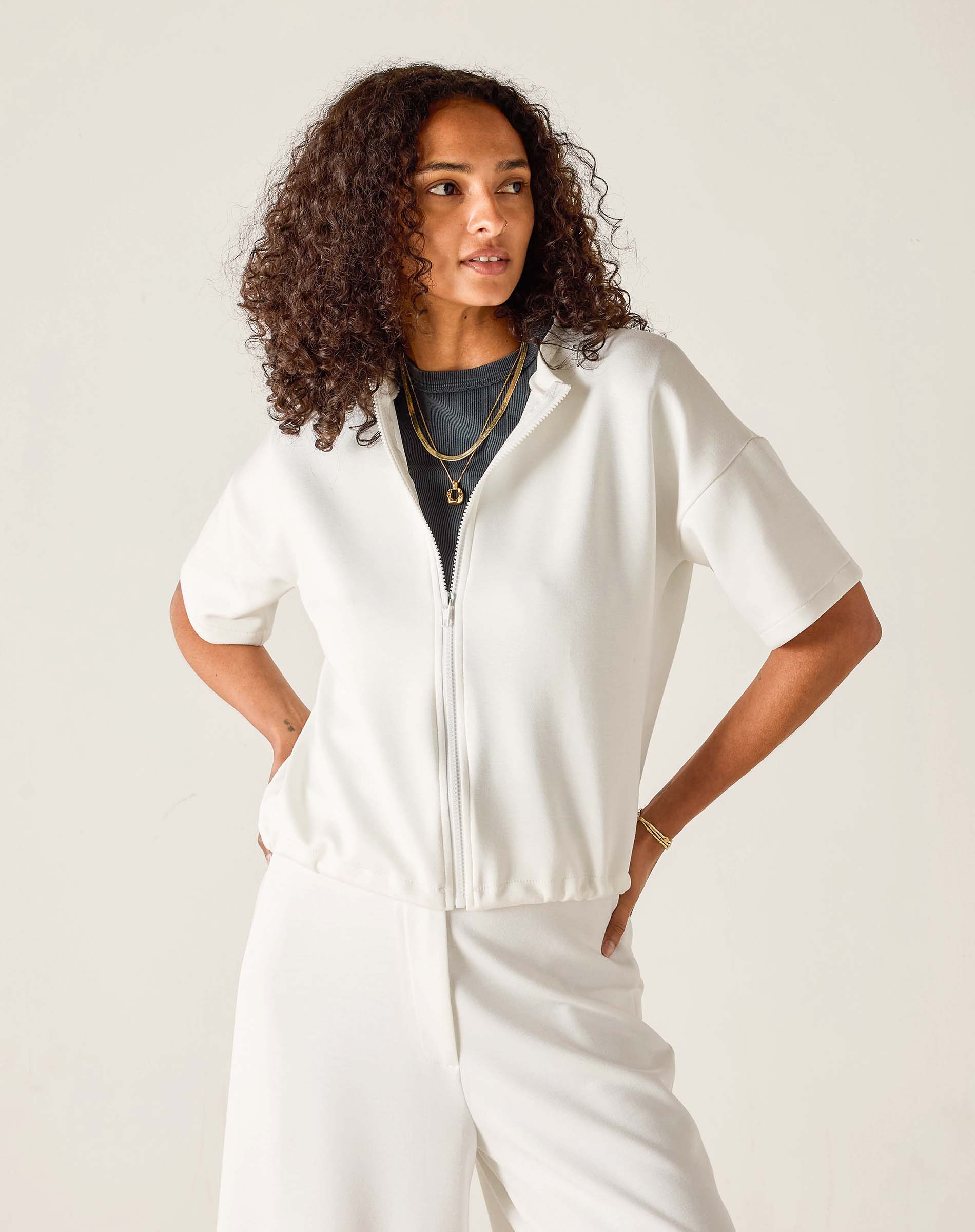 Woman wearing a white zip-up top and pants against a plain background