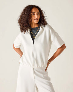 Woman wearing a white zip-up top and pants against a plain background