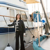 Woman standing on a boat deck with a white and blue striped boat in the background