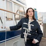 Woman wearing a navy blue jacket with white accents near a boat