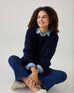 smiling woman showcasing mersea sol mate crewneck pullover in navy sitting cross legged
