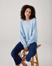 woman showcasing mersea sol mate crewneck pullover in snowflake sitting on stool