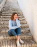 smiling woman wearing mersea sol mate crewneck pullover in snowflake sitting on stairs