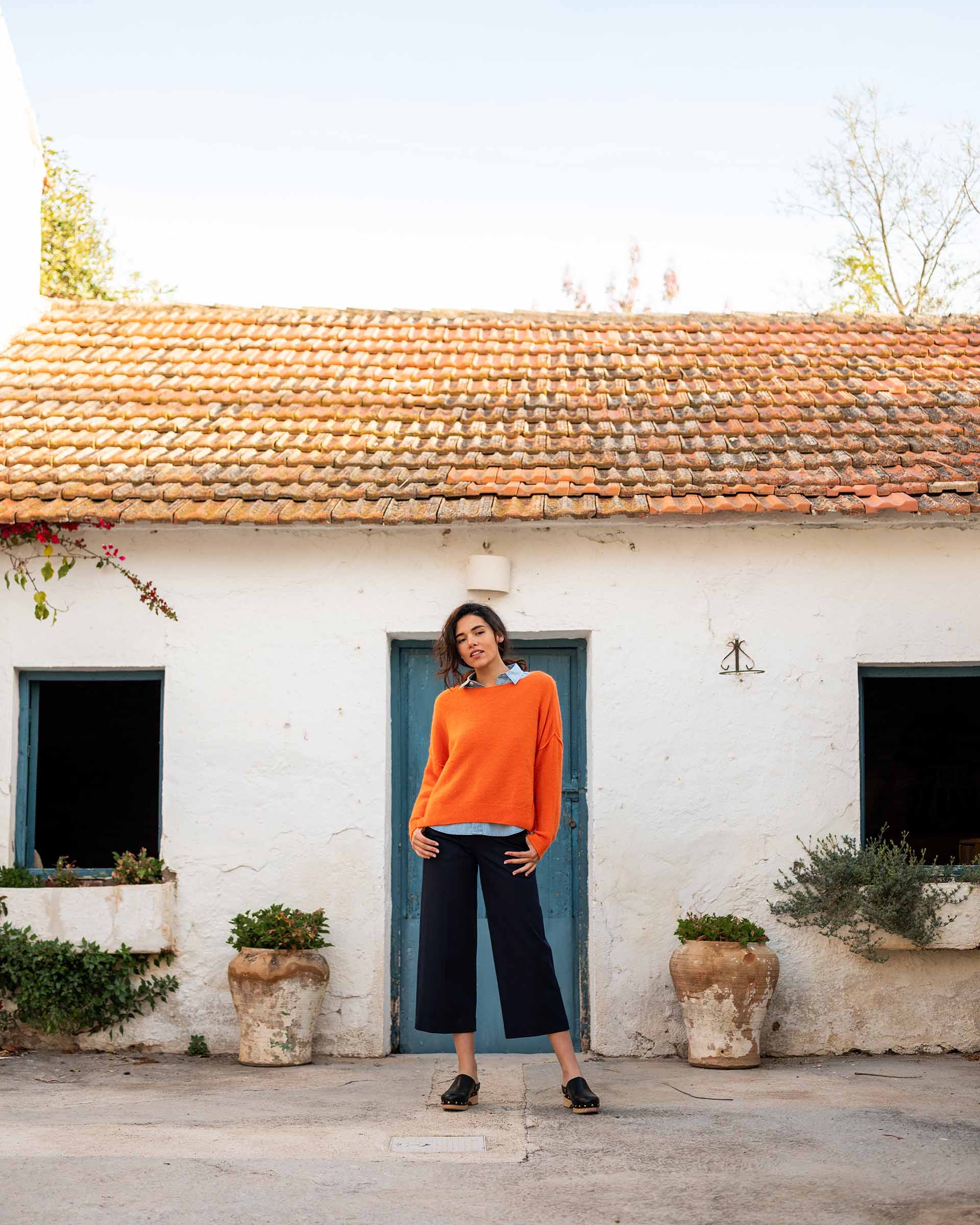 woman wearing mersea sol mate crewneck pullover in tangerine standing in front of house