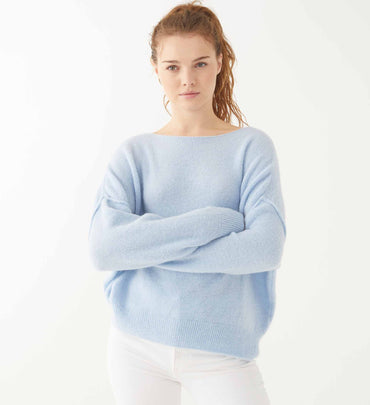 female wearing sky blue sweater over white jeans on a white background