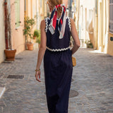 Woman in a navy dress with a colorful scarf walking down a sunlit street.
