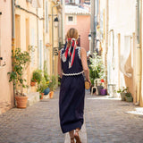 Woman in a navy dress with a red and white scarf walking down a narrow street in a European town.