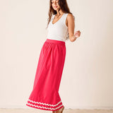 Woman wearing a white top and pink skirt with white trim on a beige background