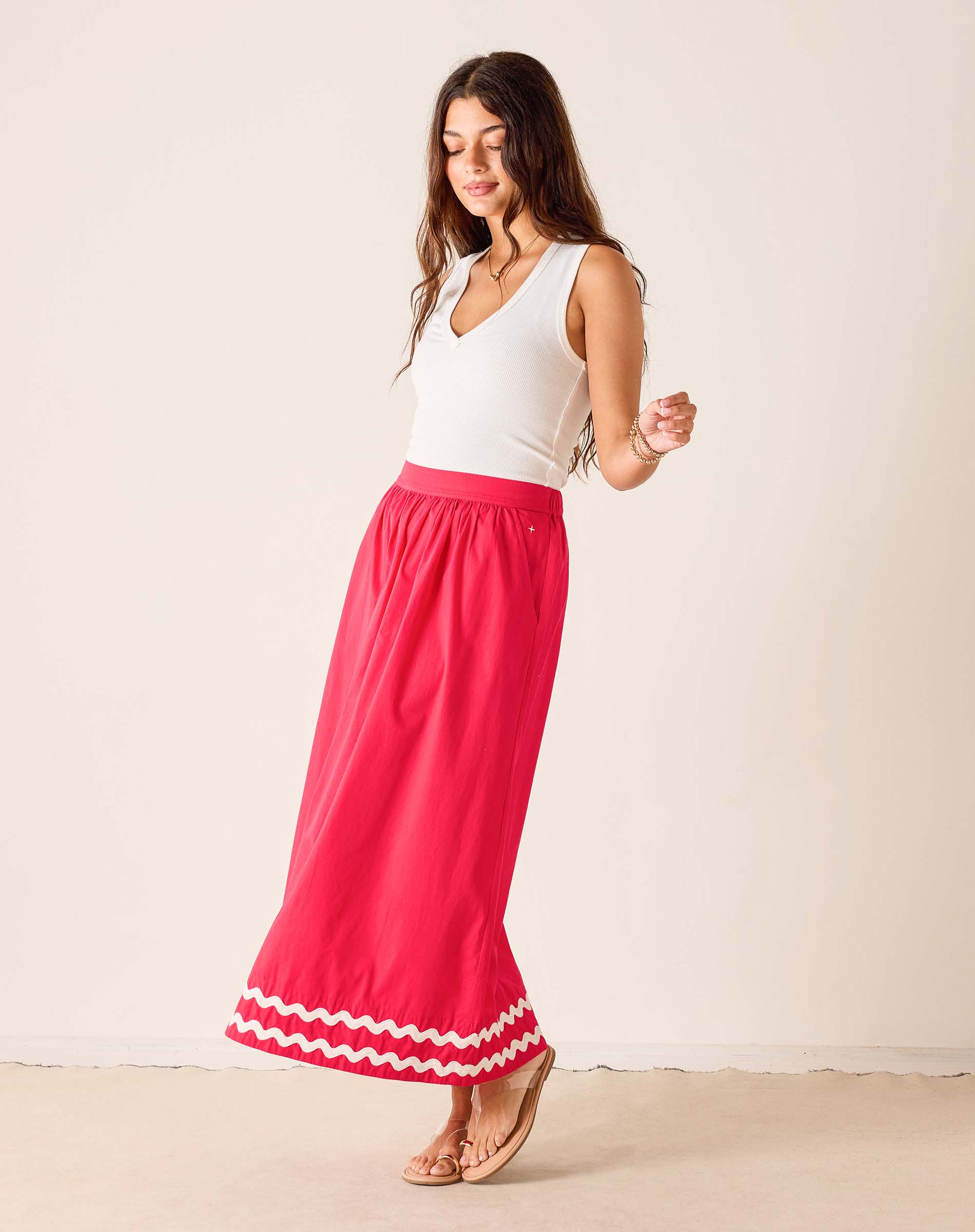 Woman wearing a white top and pink skirt with white trim on a beige background