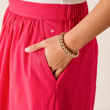 Person wearing a red skirt with a gold bracelet on a neutral background