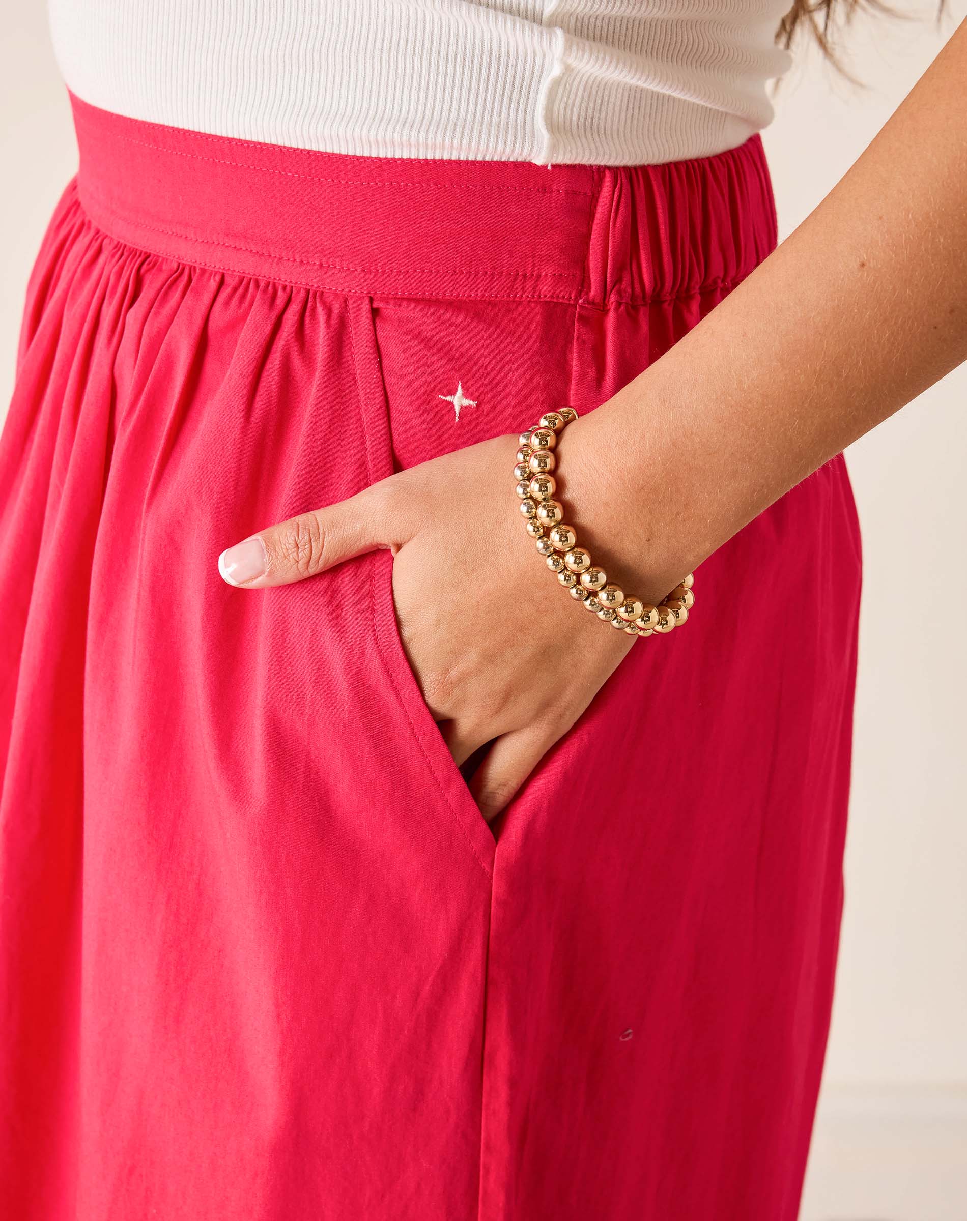 Person wearing a red skirt with a gold bracelet on a neutral background