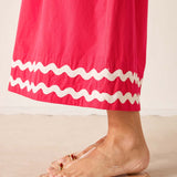 Person wearing a pink skirt with white ruffle hem and clear sandals on a beige background