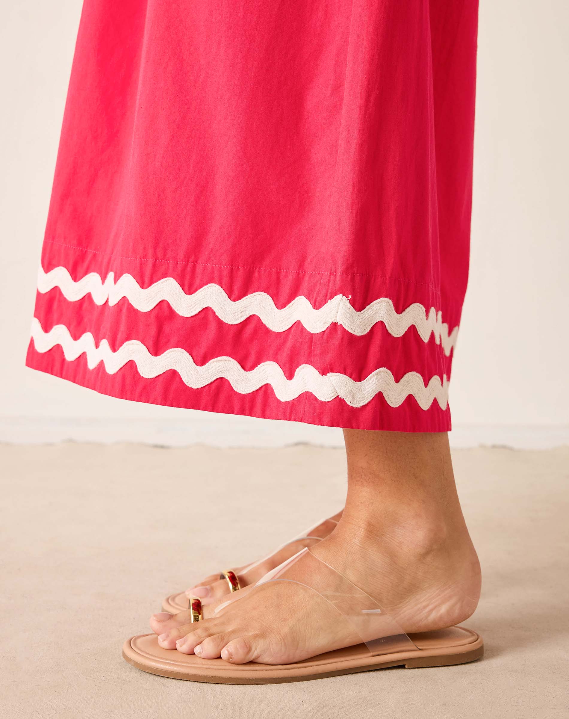 Person wearing a pink skirt with white ruffle hem and clear sandals on a beige background
