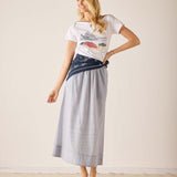 Woman wearing a white t-shirt with a graphic design and a long gray skirt on a plain background
