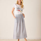 Woman wearing a graphic t-shirt and light blue skirt on a plain background
