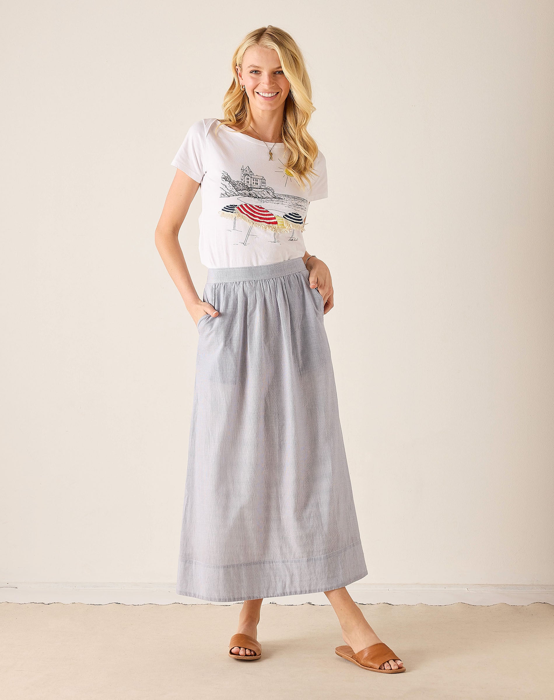 Woman wearing a graphic t-shirt and light blue skirt on a plain background