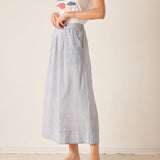 Woman wearing a white top and light blue skirt on a plain background