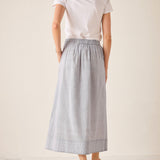 Woman wearing a white top and light blue skirt on a plain background