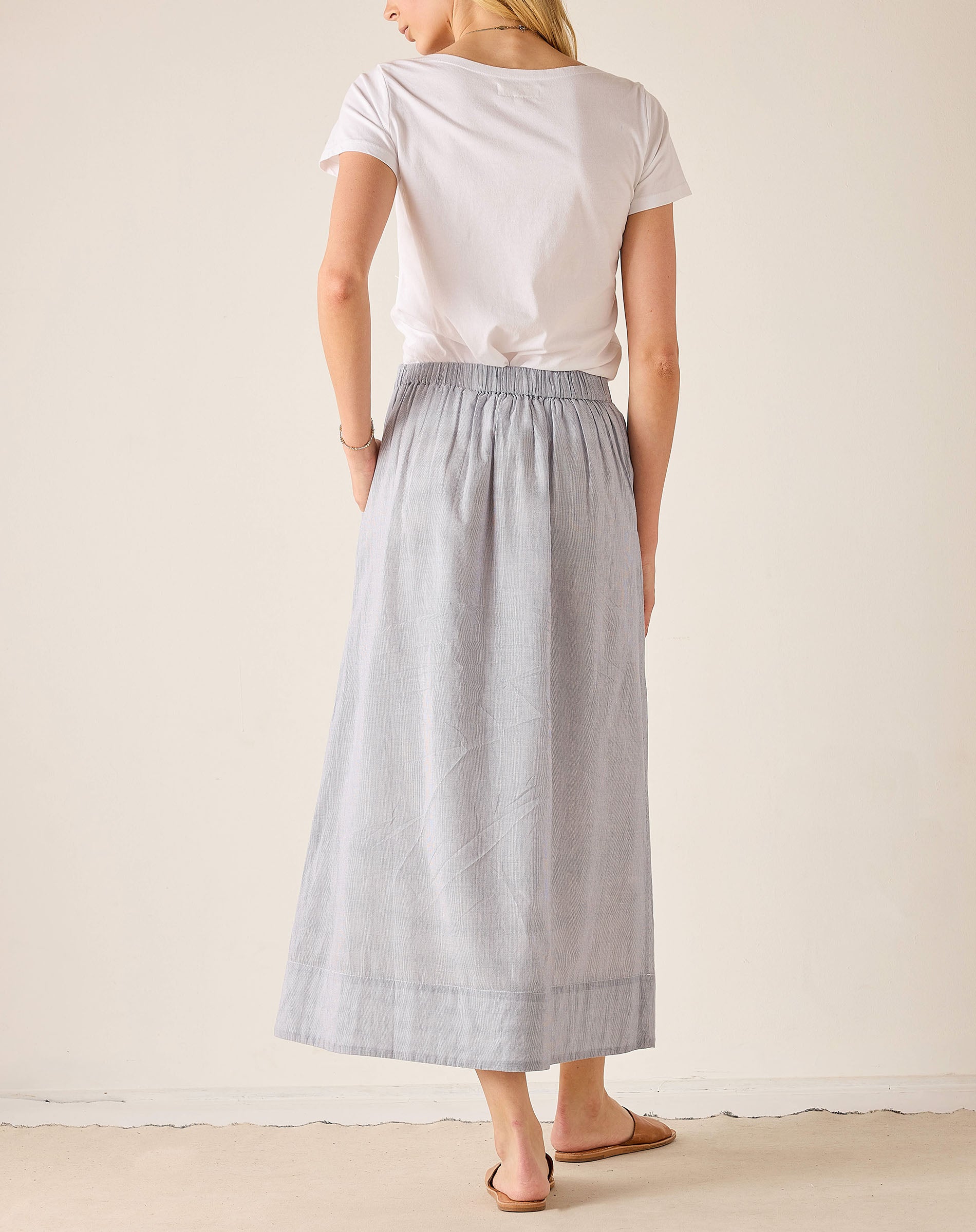 Woman wearing a white top and light blue skirt on a plain background
