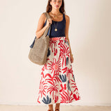 Woman wearing a red and blue patterned skirt holding a straw bag against a plain background