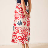 Person wearing a long, patterned skirt with red and blue floral design on a plain background