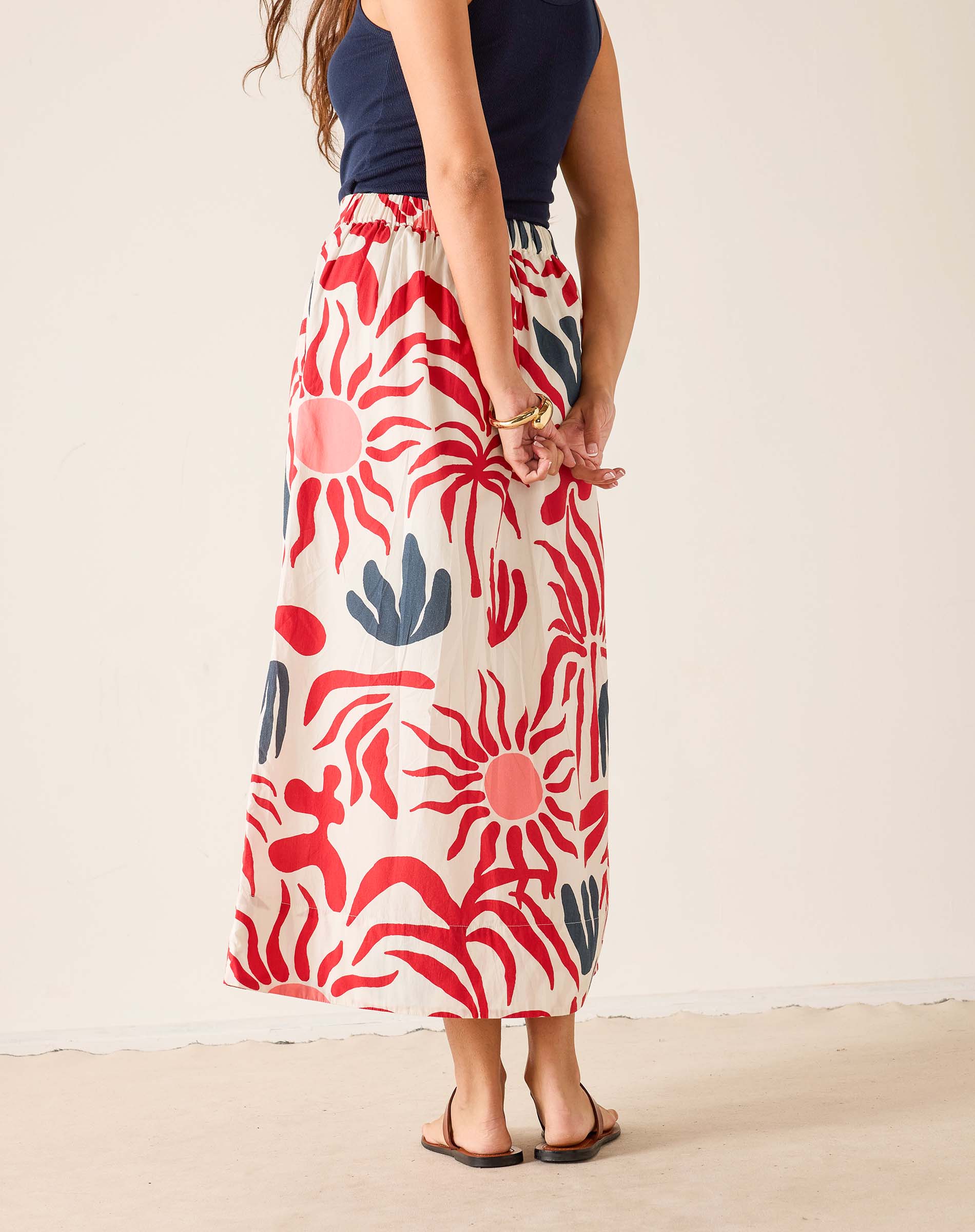 Person wearing a long, patterned skirt with red and blue floral design on a plain background