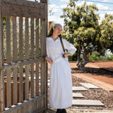 Woman in Yard by Gate Wearing Long White Skirt and Longsleeve White Shirt Set