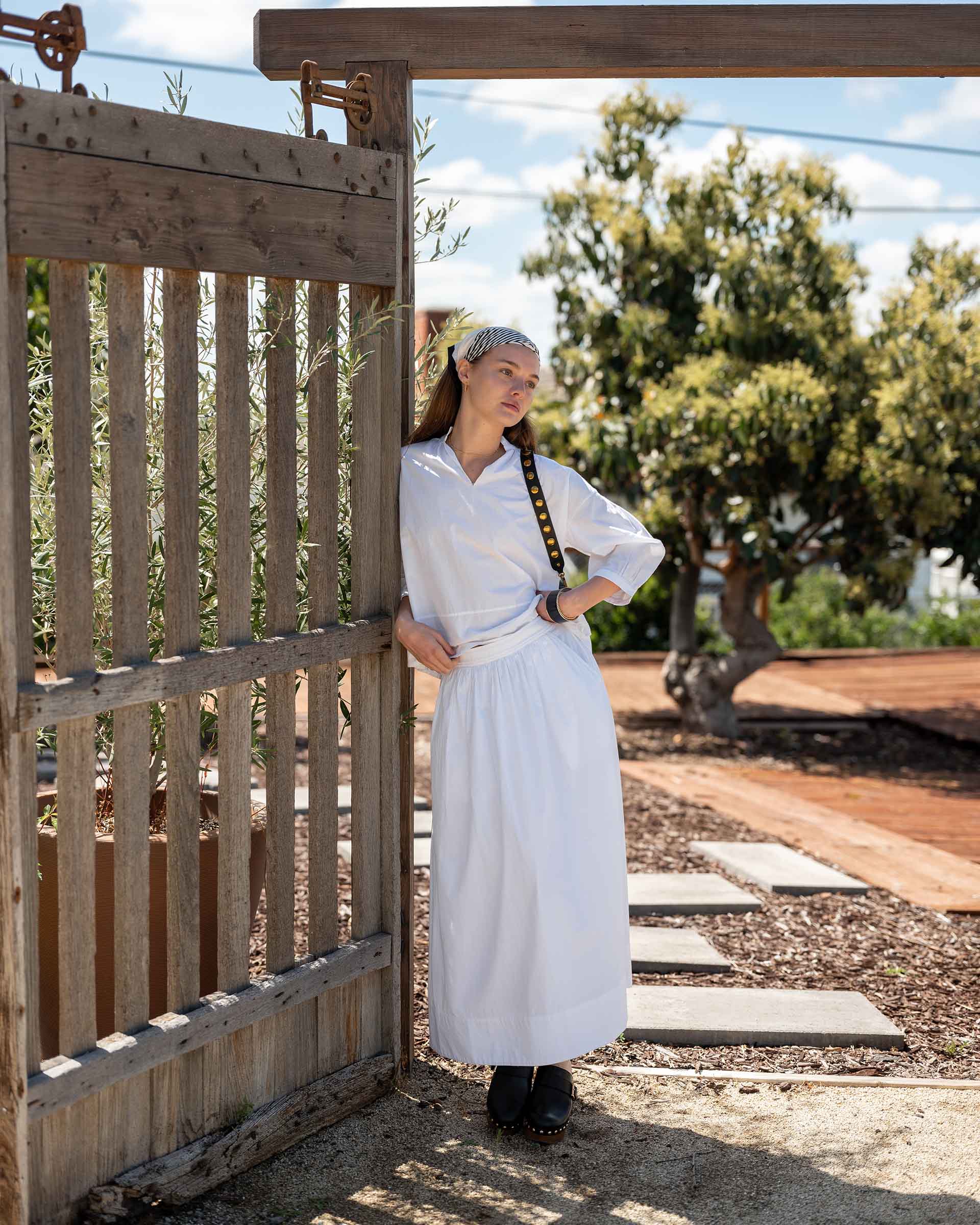 Woman in Yard by Gate Wearing Long White Skirt and Longsleeve White Shirt Set