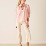 Woman wearing a pink blouse and white pants against a plain background