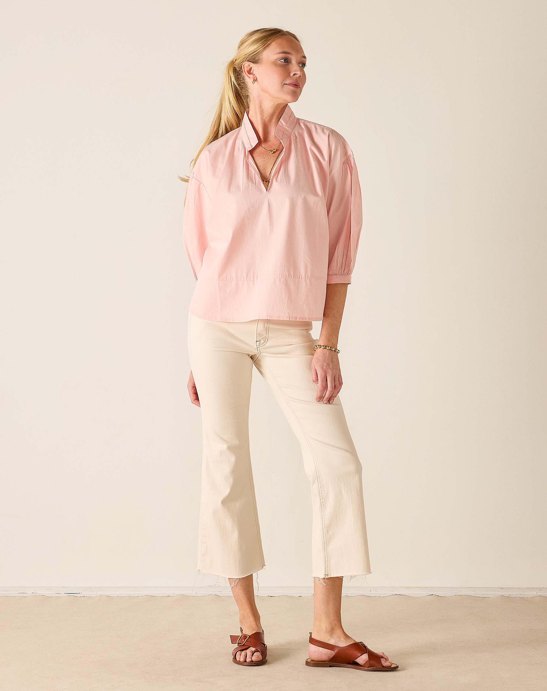 Woman wearing a pink blouse and white pants against a plain background
