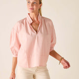 Woman wearing a light pink blouse and beige pants against a plain background