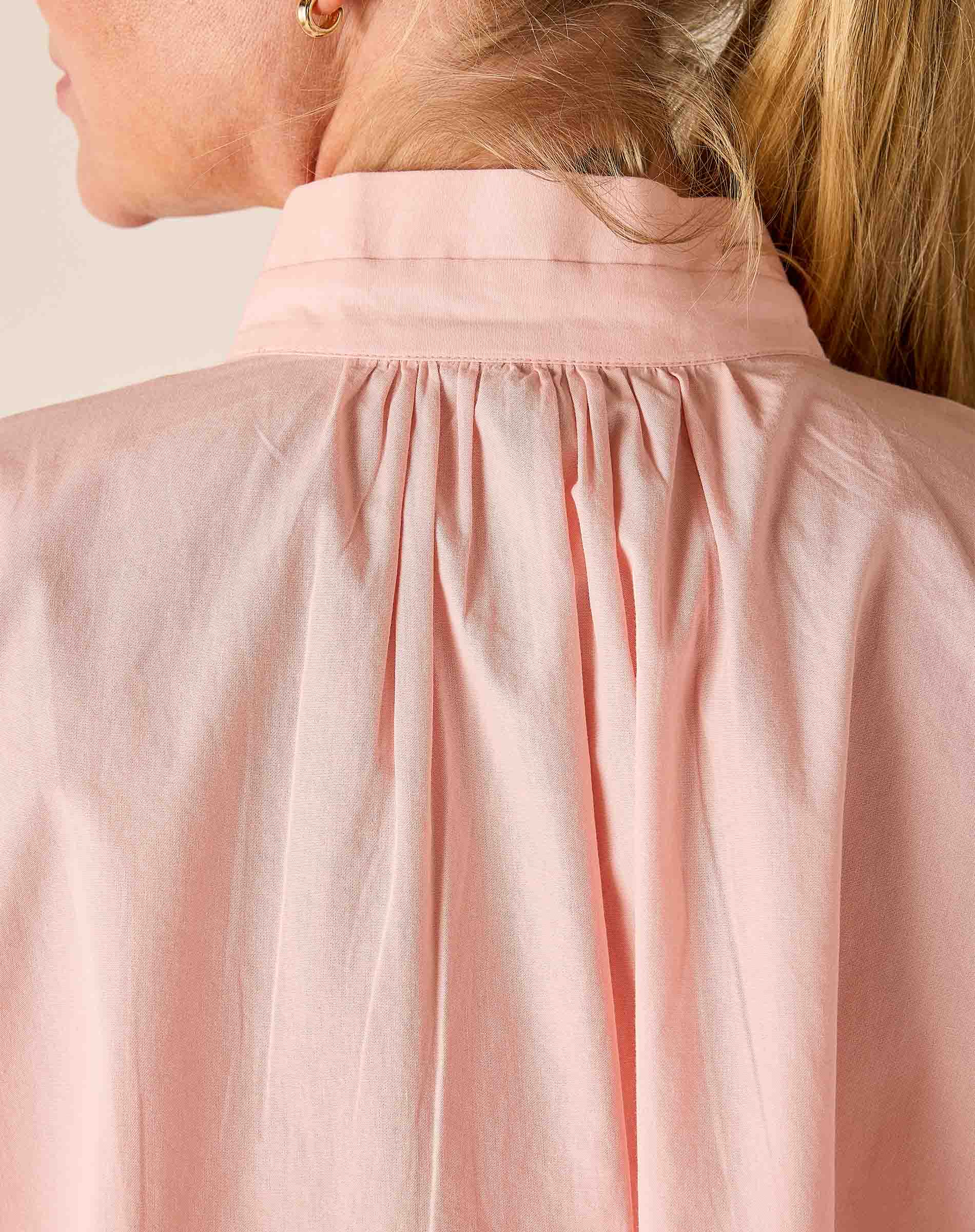 Close-up of a person wearing a light pink blouse with a neutral background