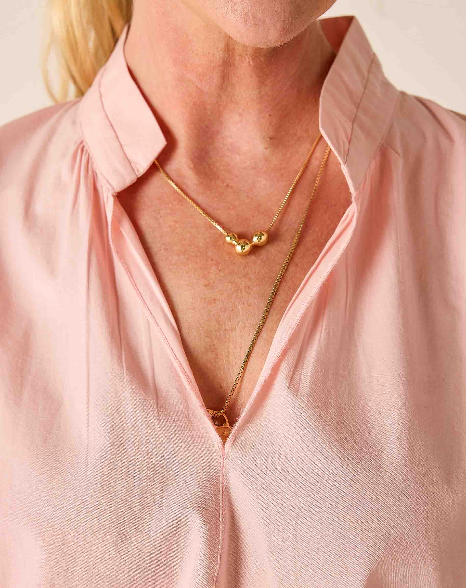 Person wearing a gold necklace with a pink shirt