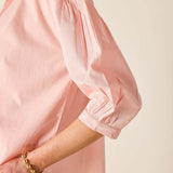 Close-up of a person wearing a pink blouse with balloon sleeves on a beige background