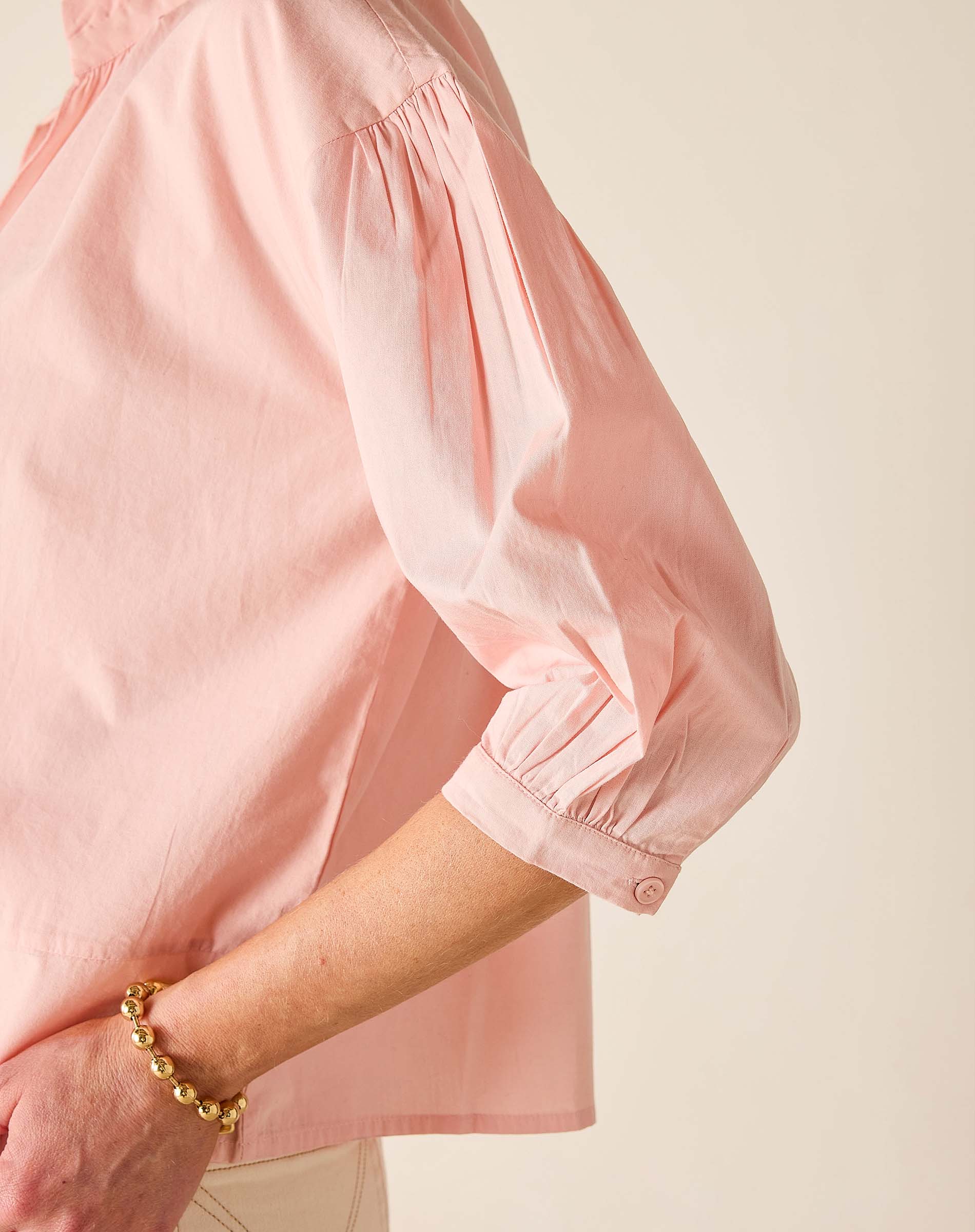 Close-up of a person wearing a pink blouse with balloon sleeves on a beige background