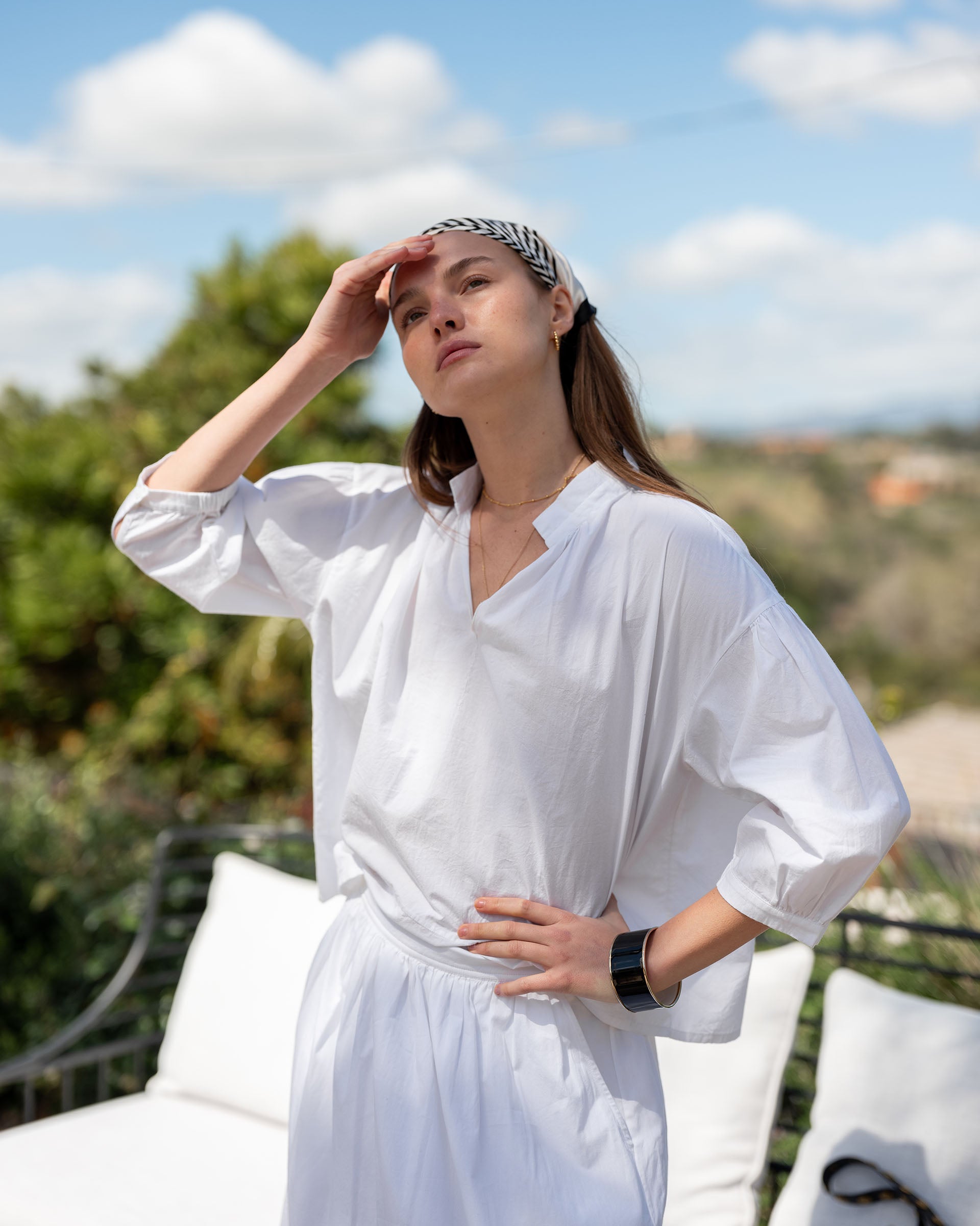 Woman in a white outfit standing outdoors with a scenic background