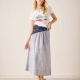 Woman wearing a graphic t-shirt and long light gray skirt against a plain background