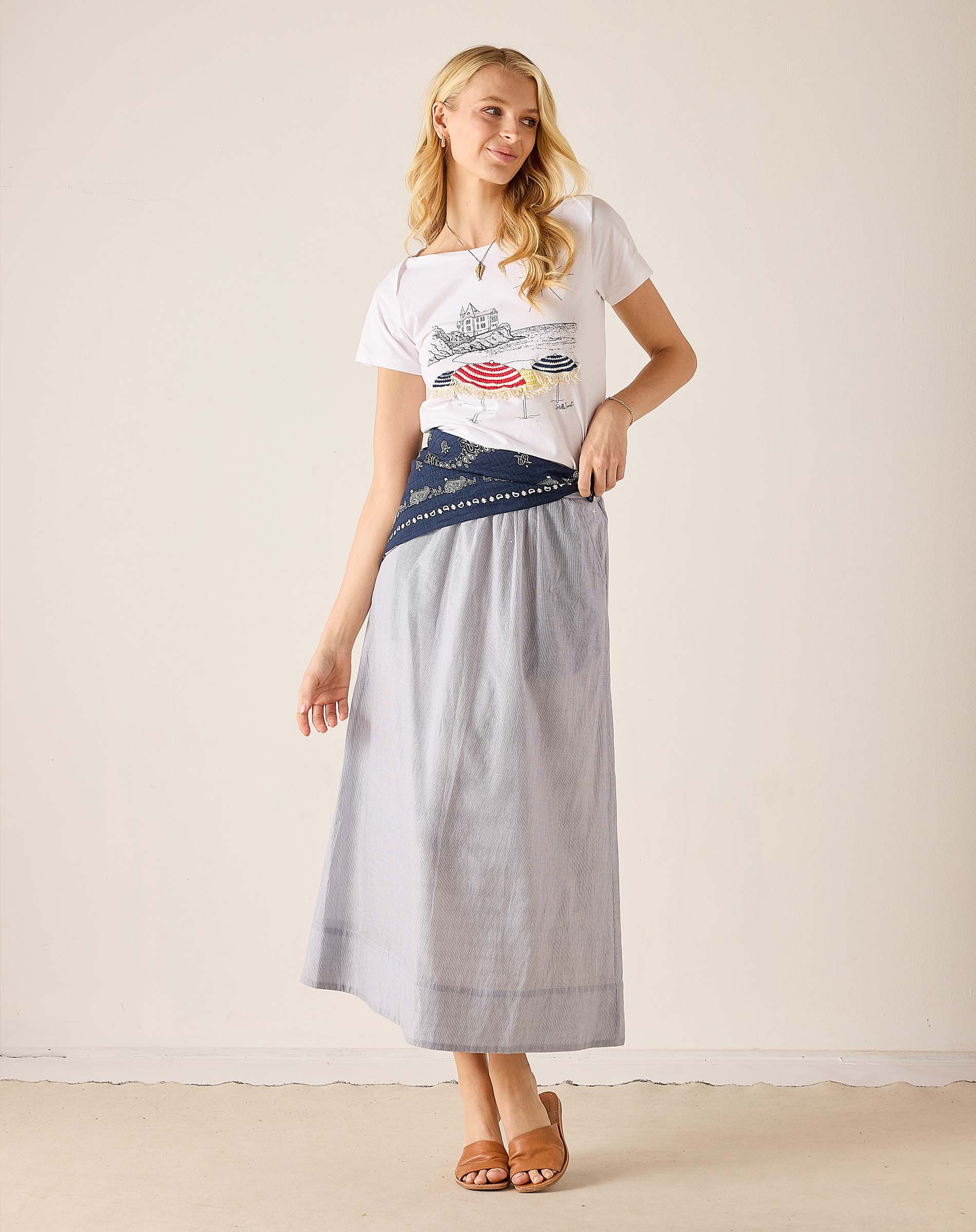 Woman wearing a graphic t-shirt and long light gray skirt against a plain background