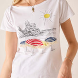 White t-shirt with beach scene design featuring umbrellas and a castle.