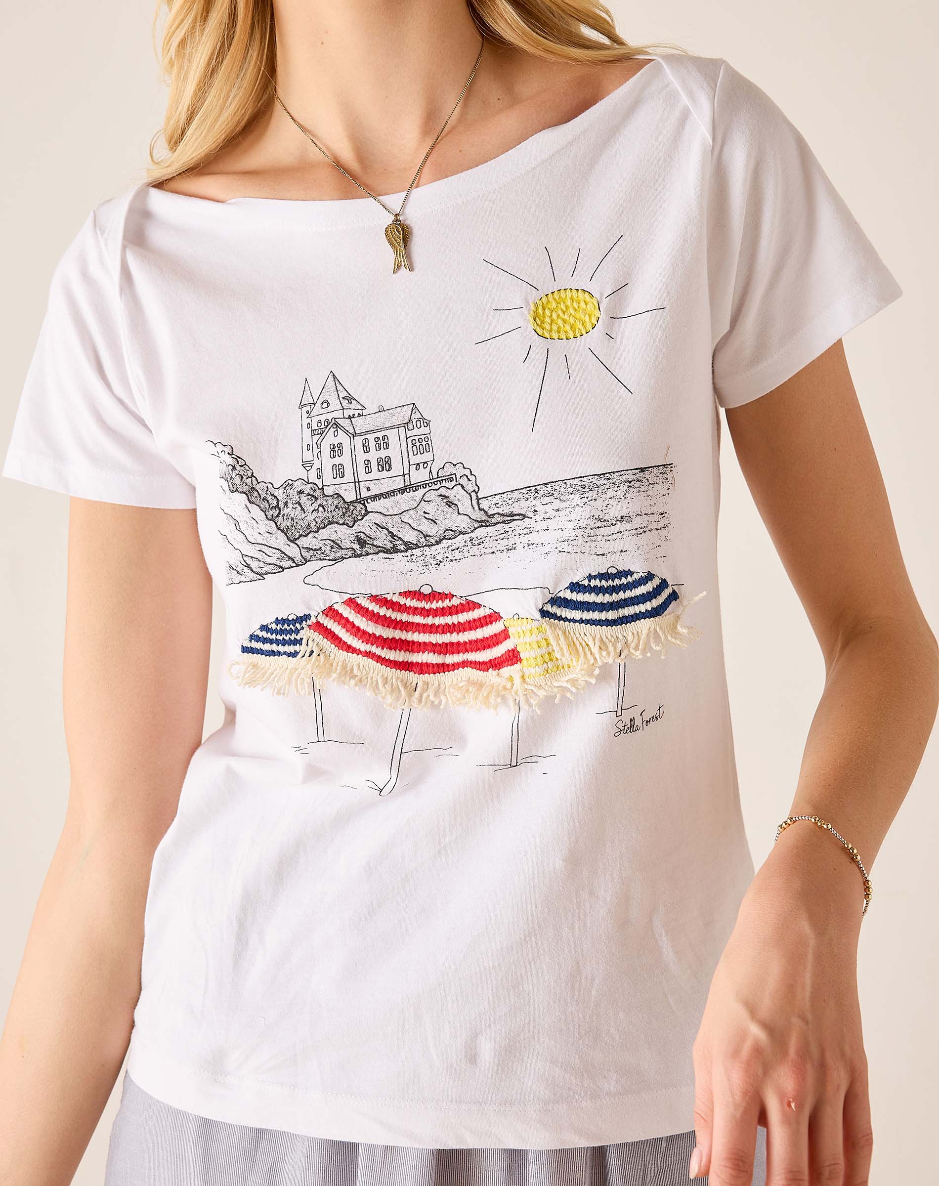 White t-shirt with beach scene design featuring umbrellas and a castle.