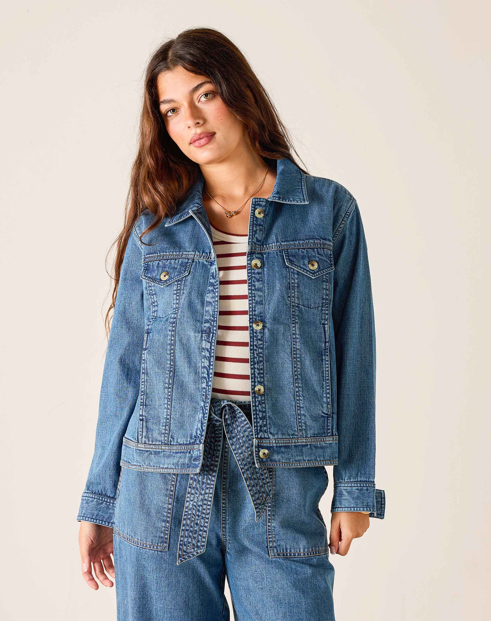 Woman wearing a denim jacket and striped shirt against a plain background