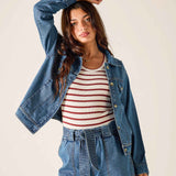 Woman wearing a denim jacket, striped shirt, and blue pants on a plain background