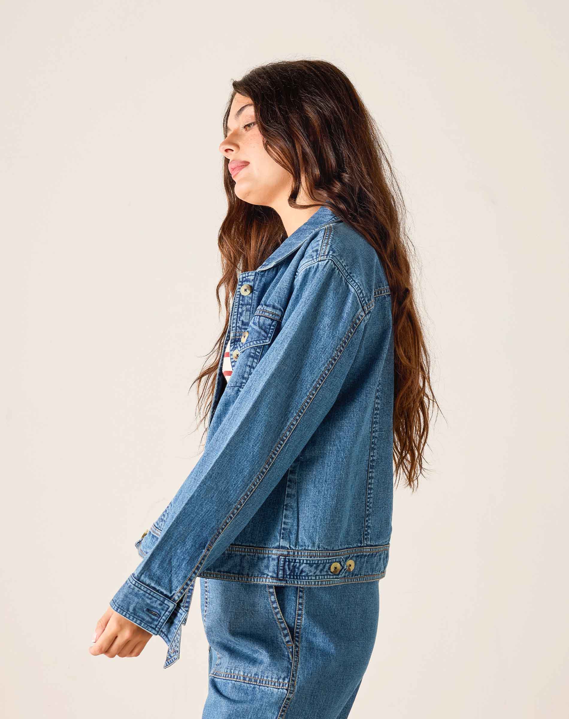 Person wearing a blue denim jacket and pants against a plain background