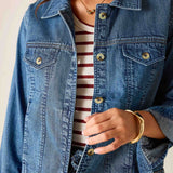 Person wearing a blue denim jacket over a striped shirt with a neutral background