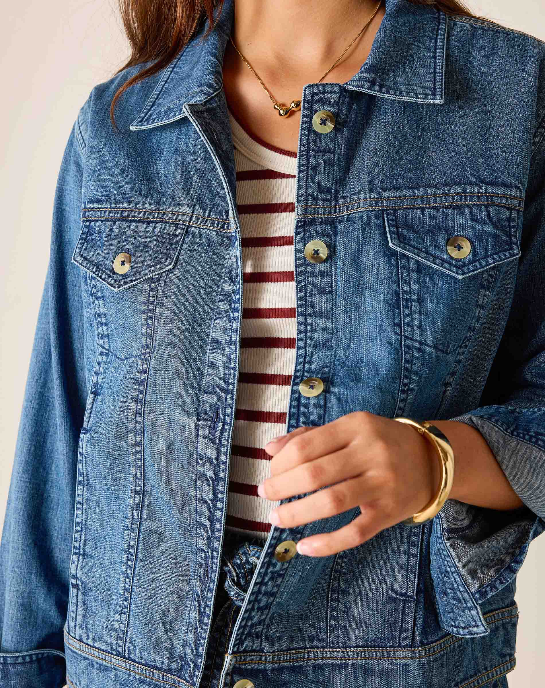 Person wearing a blue denim jacket over a striped shirt with a neutral background