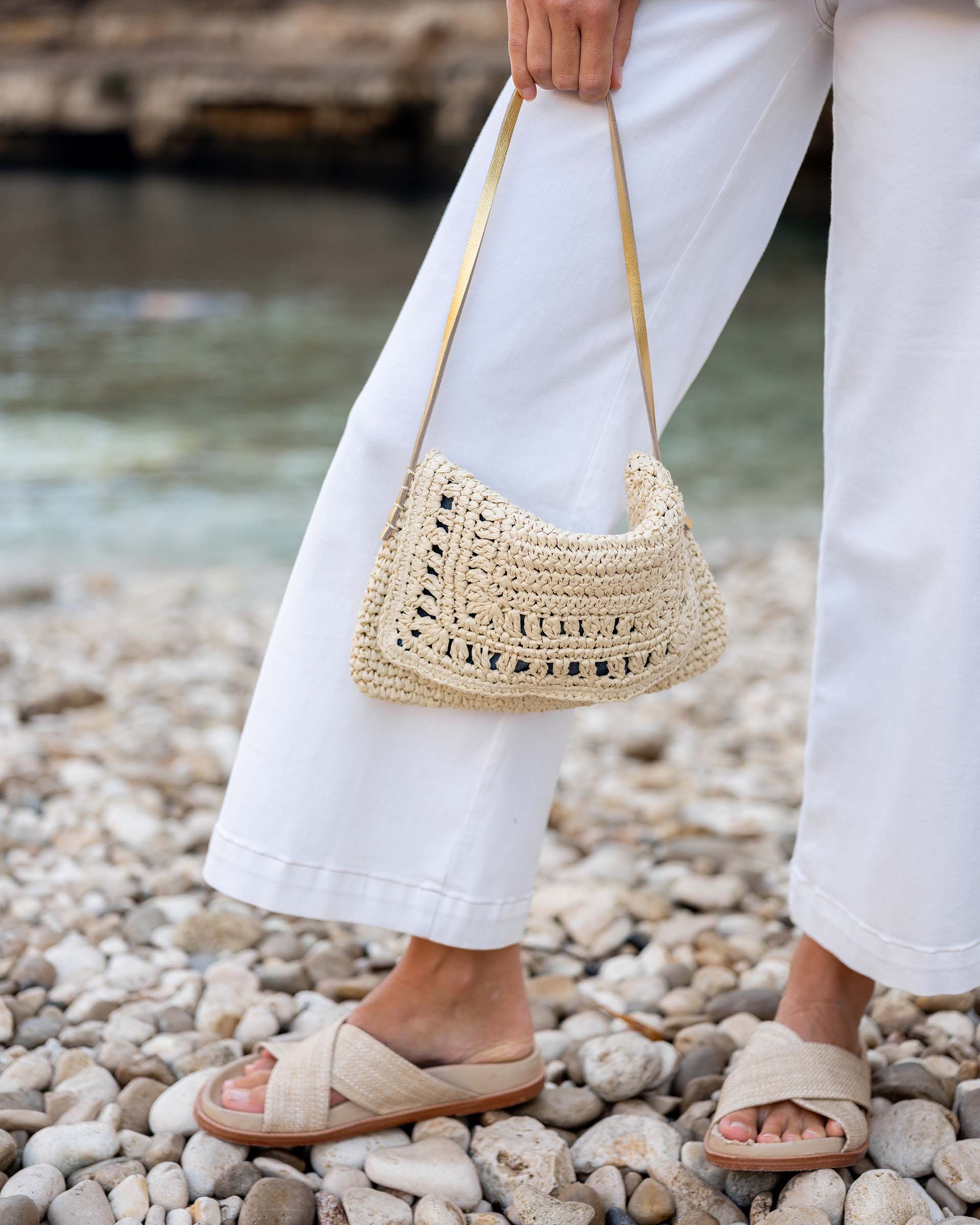 close up image of woman holding sun chaser straw pochette with white jeans on